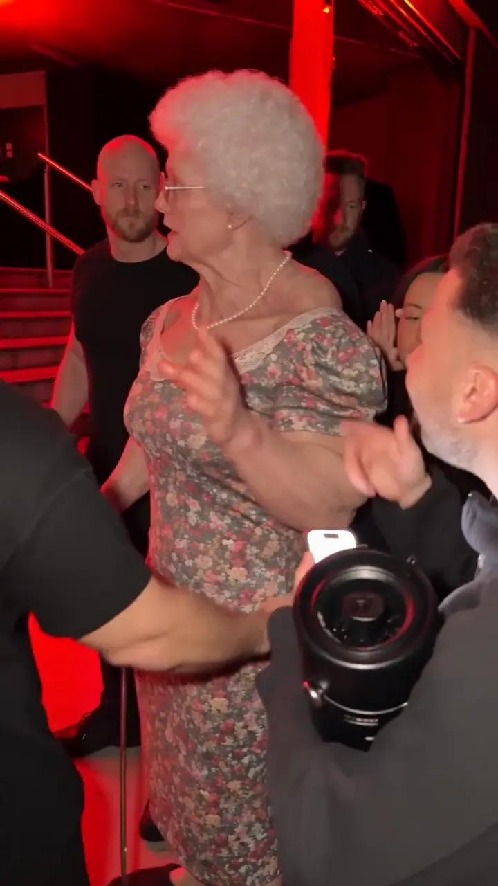 Bulin 47 AI video trend: a grandmother freestyles at the red-lit door while a fan holds up the speaker